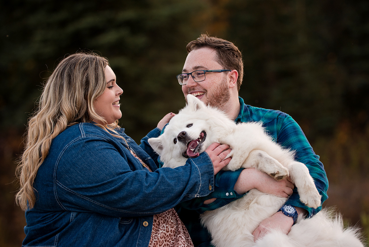 Couple enjoying an engagement photo session in the park with their Samoyed dog.