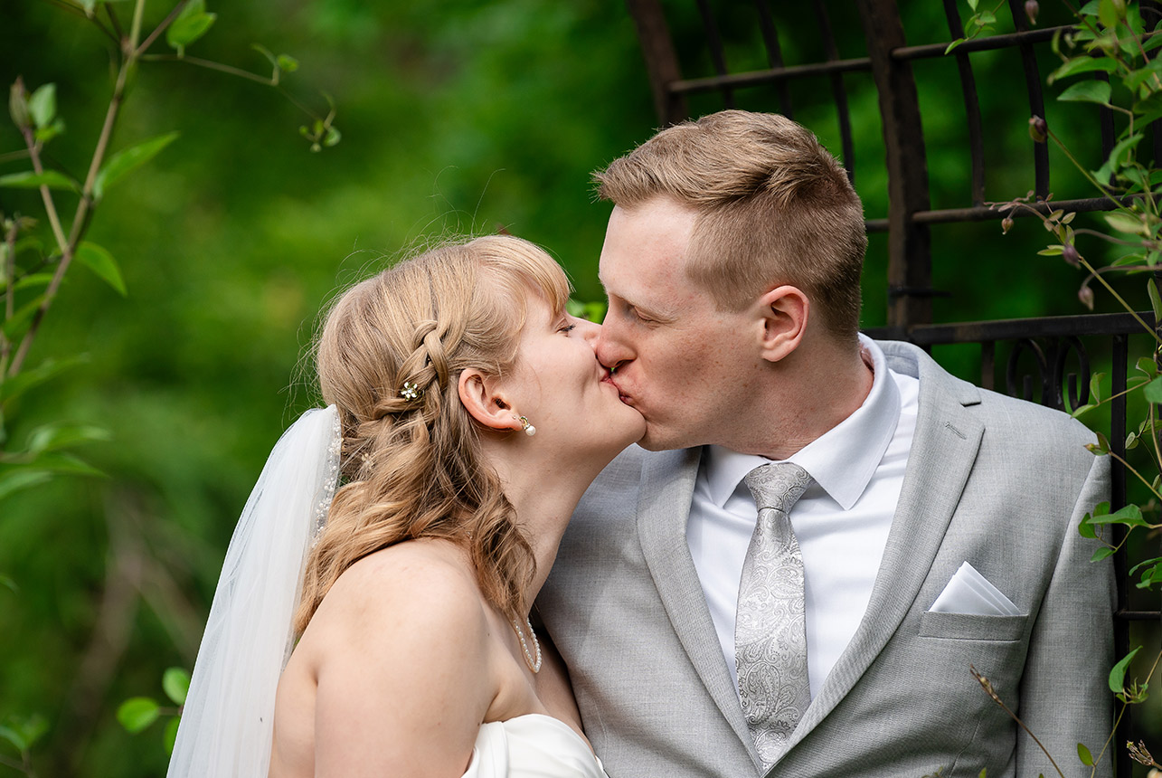 erin-eric-archway-kiss-smeltzer Bride and groom kissing under ivy-covered arch