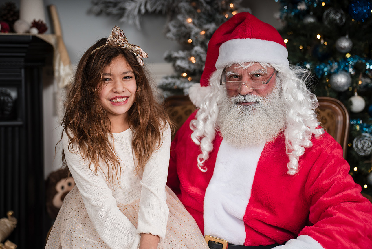 Young girl in cream dress smiling next to Santa Claus during a festive studio session