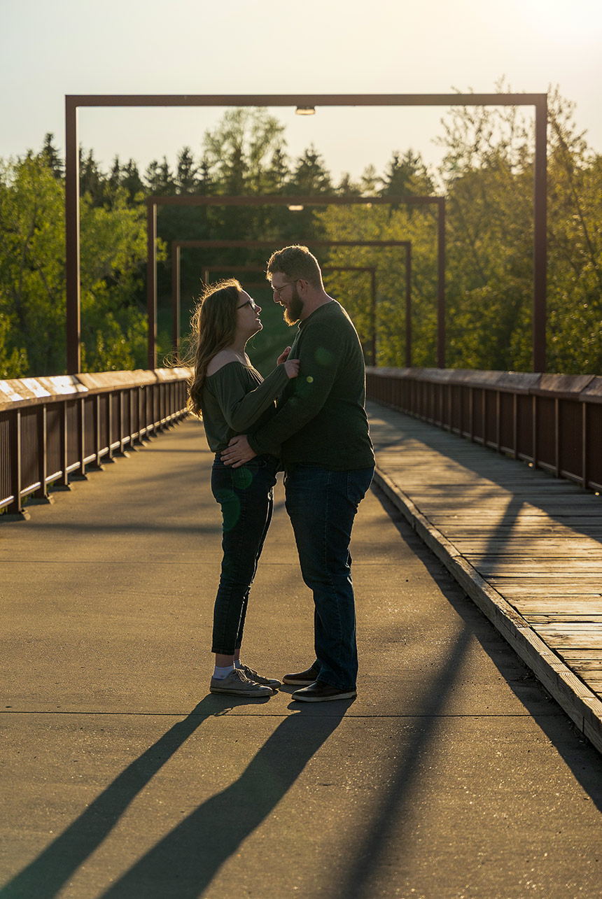Couple standing face to face on a bridge during golden hour with long shadows and soft sunlight in Edmonton Alberta
