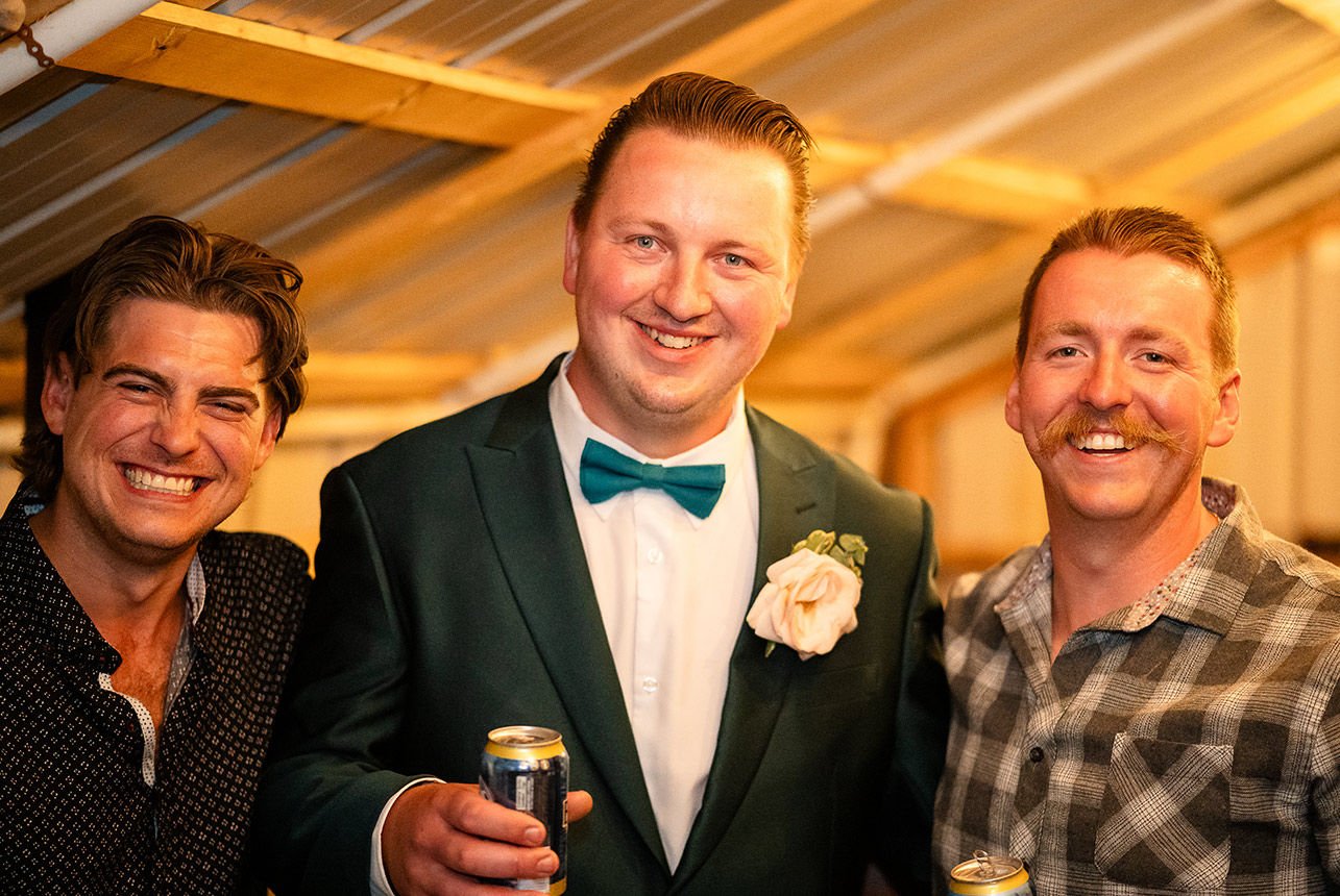 The groom stands on stage with his two best friends during the evening celebration, sharing laughter and memories