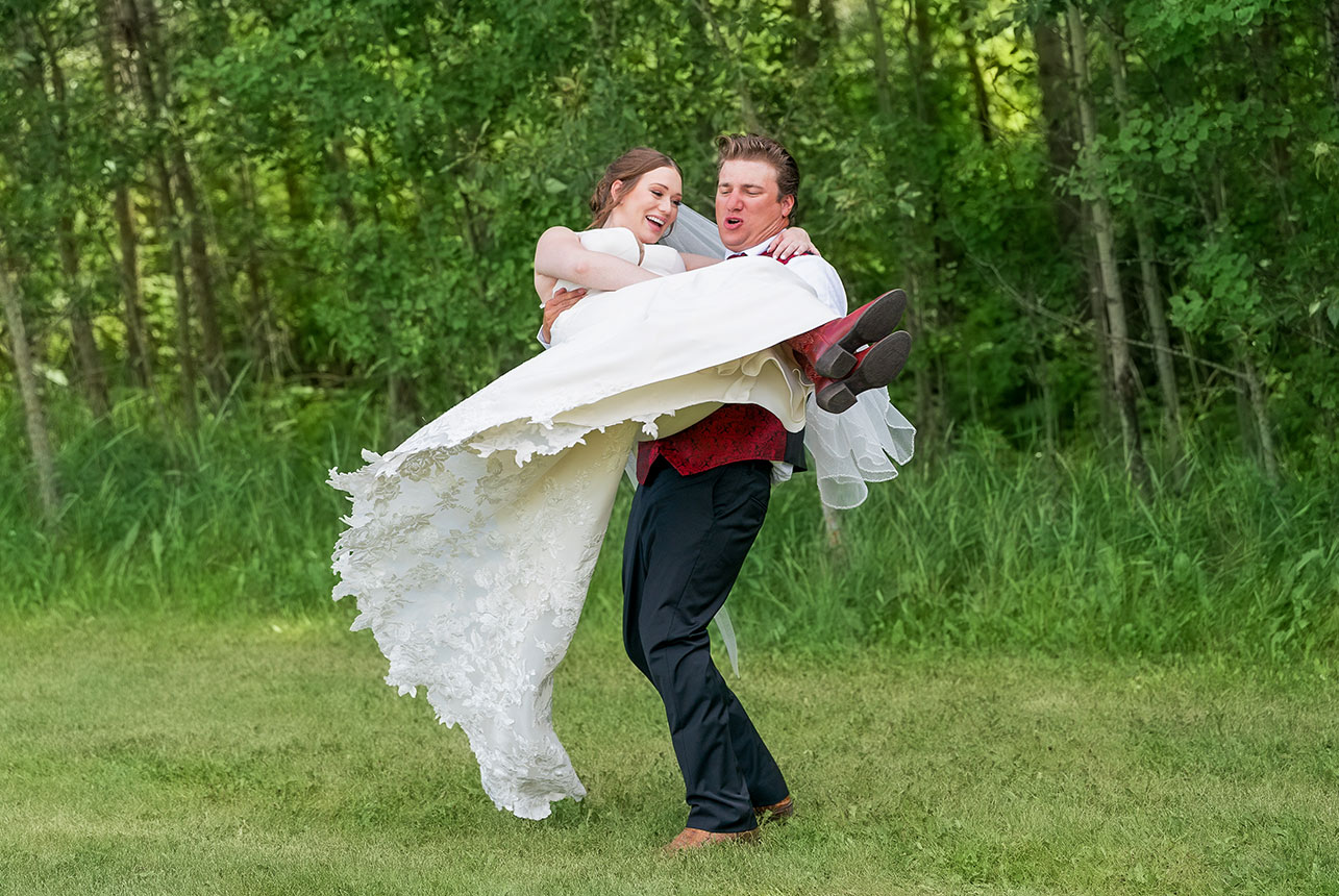 Groom twirls bride midair during joyful outdoor wedding moment
