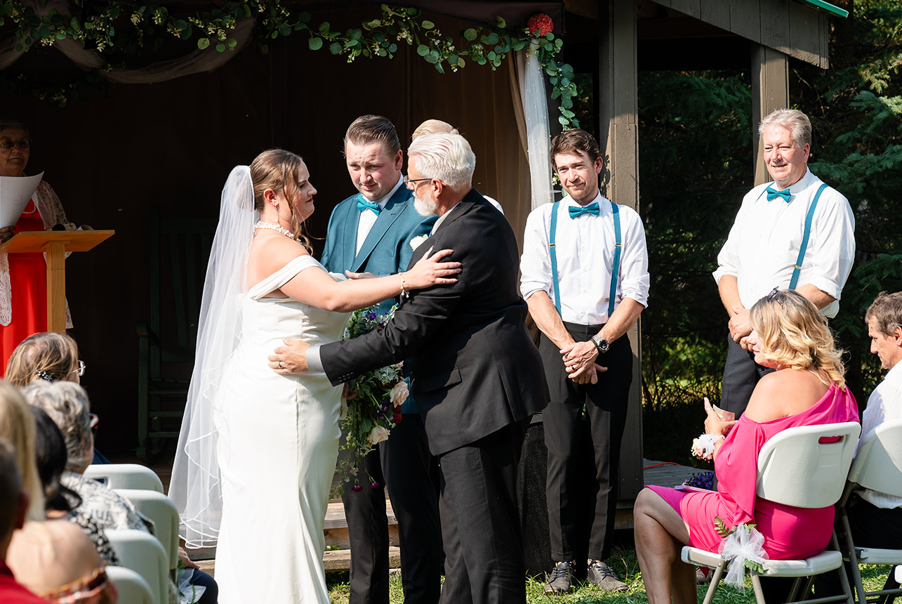 Groom shares a heartfelt hug with his daughter before turning to see his bride, standing with his three best men at the Rustic Wedding Pavilion