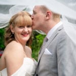 Side profile of the groom kissing his smiling bride as her veil flows during an Edmonton wedding