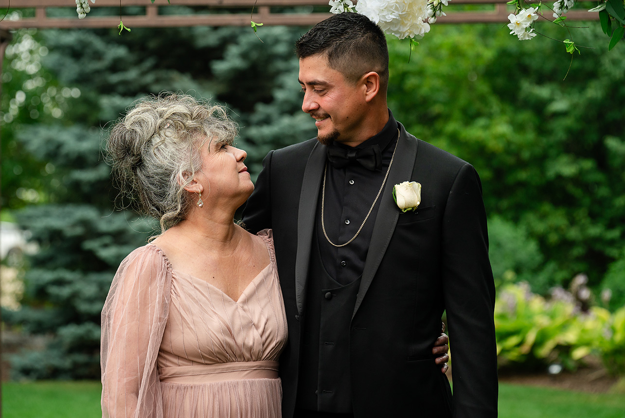 A groom and his mother sharing a heartfelt moment, looking into each other's eyes during their wedding ceremony at Greenland Botanic Gardens in Sherwood Park, near Edmonton.