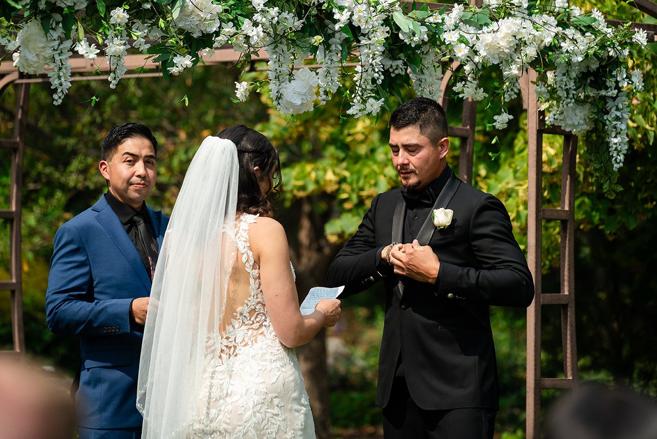 Groom reaching into his jacket to present the wedding ring while the commissioner stands by and the bride prepares to read her vows.