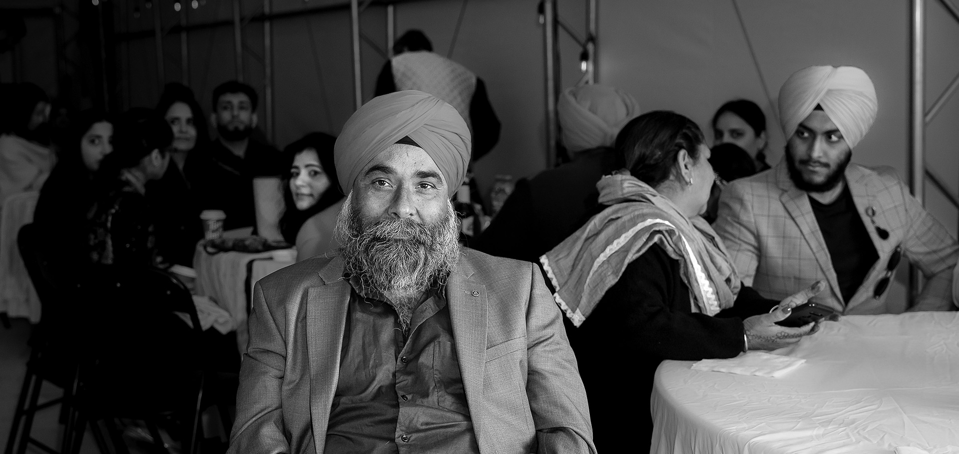 grooms-father-smiling-sikh-wedding-edmonton Groom’s father smiles with eyes warmly during the Sikh wedding reception in Edmonton, with guests blurred in the background