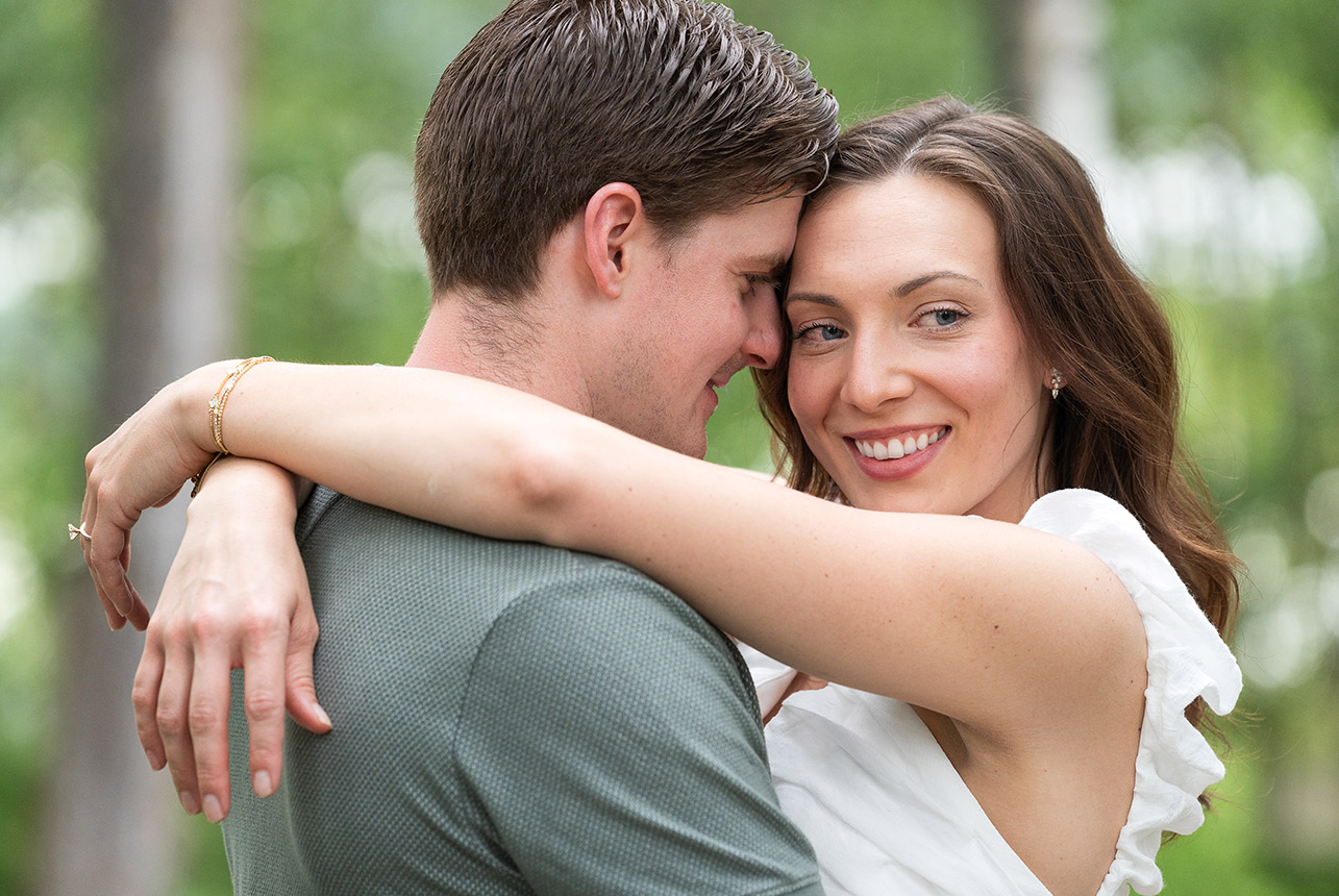 joyful forest embrace summer engagement Couple shares a soft embrace among tall trees, smiling warmly with love in their eyes