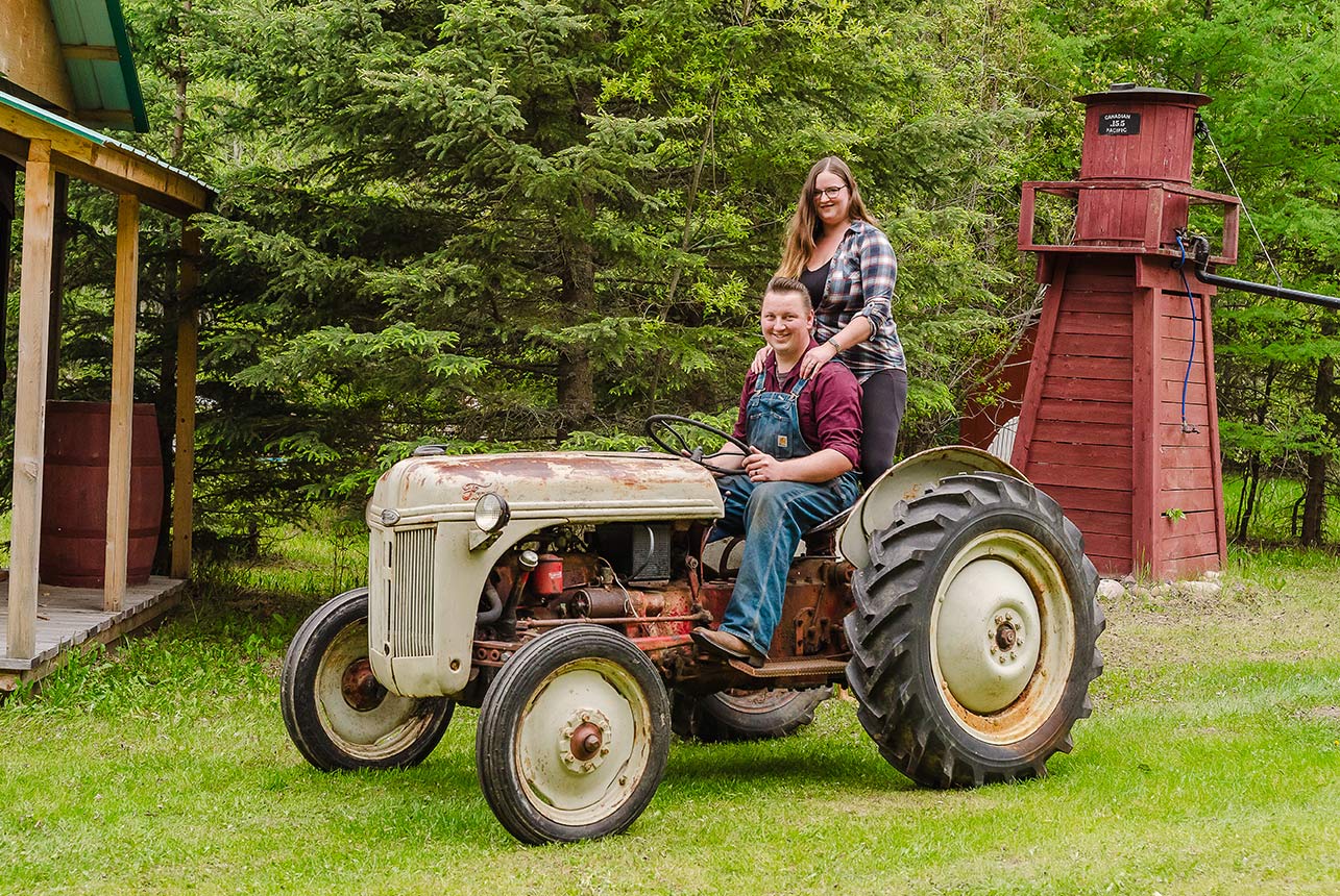 Man driving a vintage rustic tractor with his girlfriend standing on the back axle for a ride