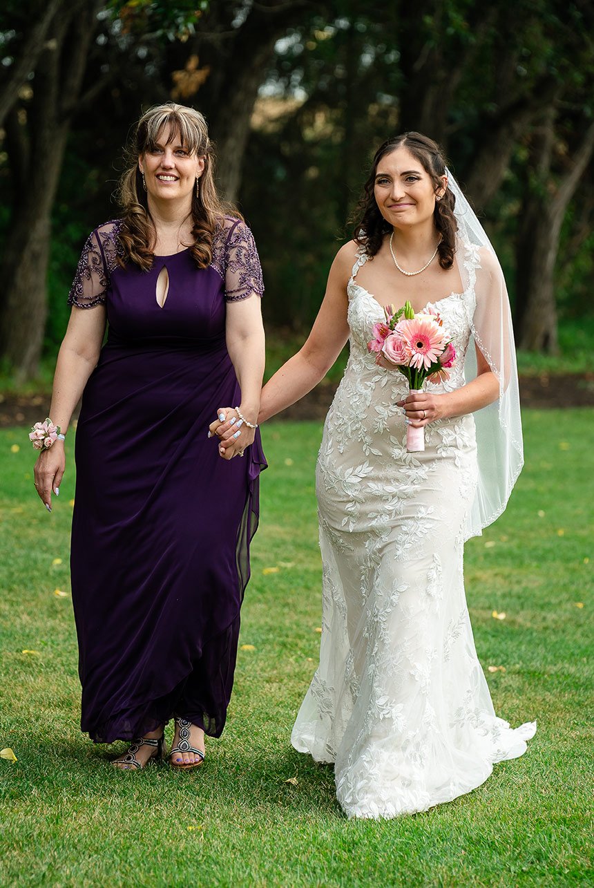 A mother holding her bride's hand as they walk towards the wedding aisle at Greenland Botanic Gardens in Sherwood Park, near Edmonton.