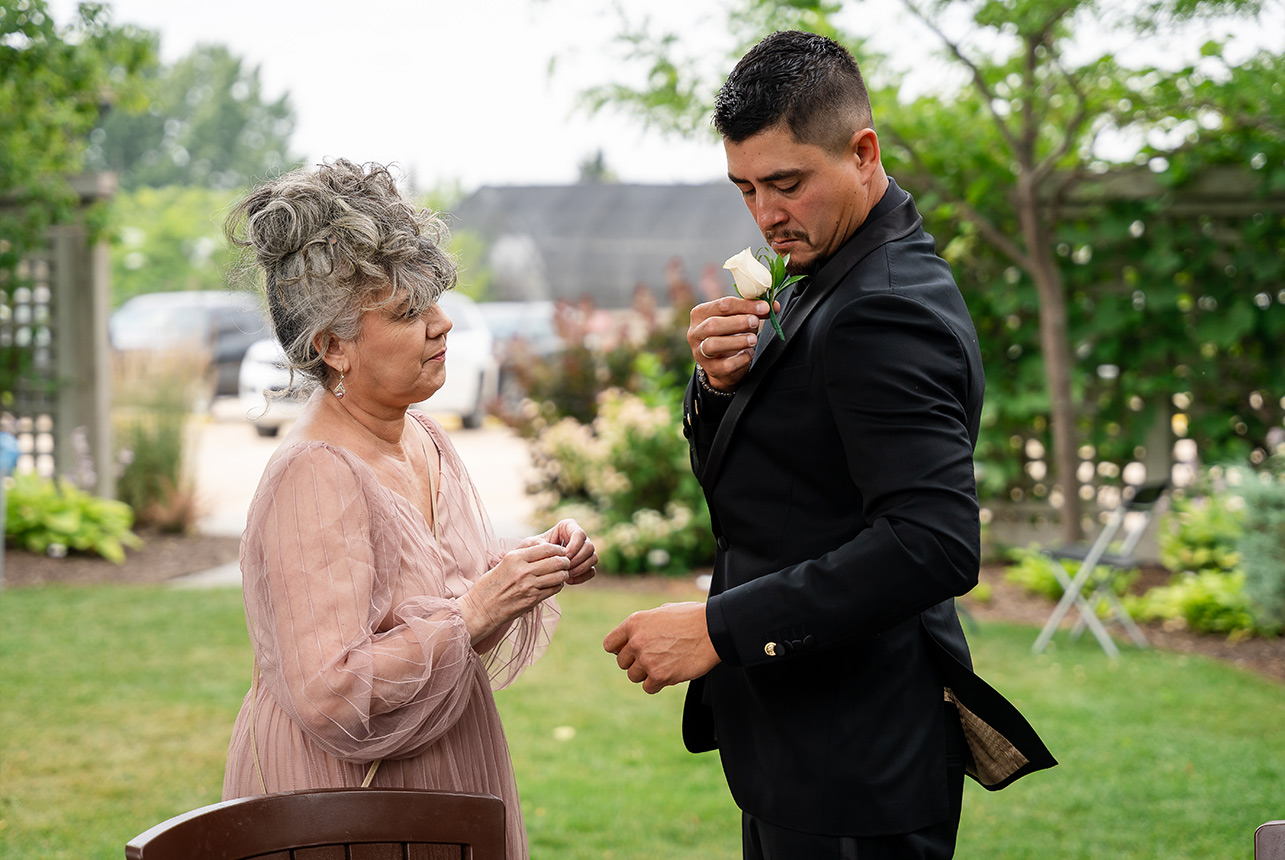 A mother assisting her son, the groom, in placing his boutonniere during an Edmonton wedding ceremony, with a pin in her hand.