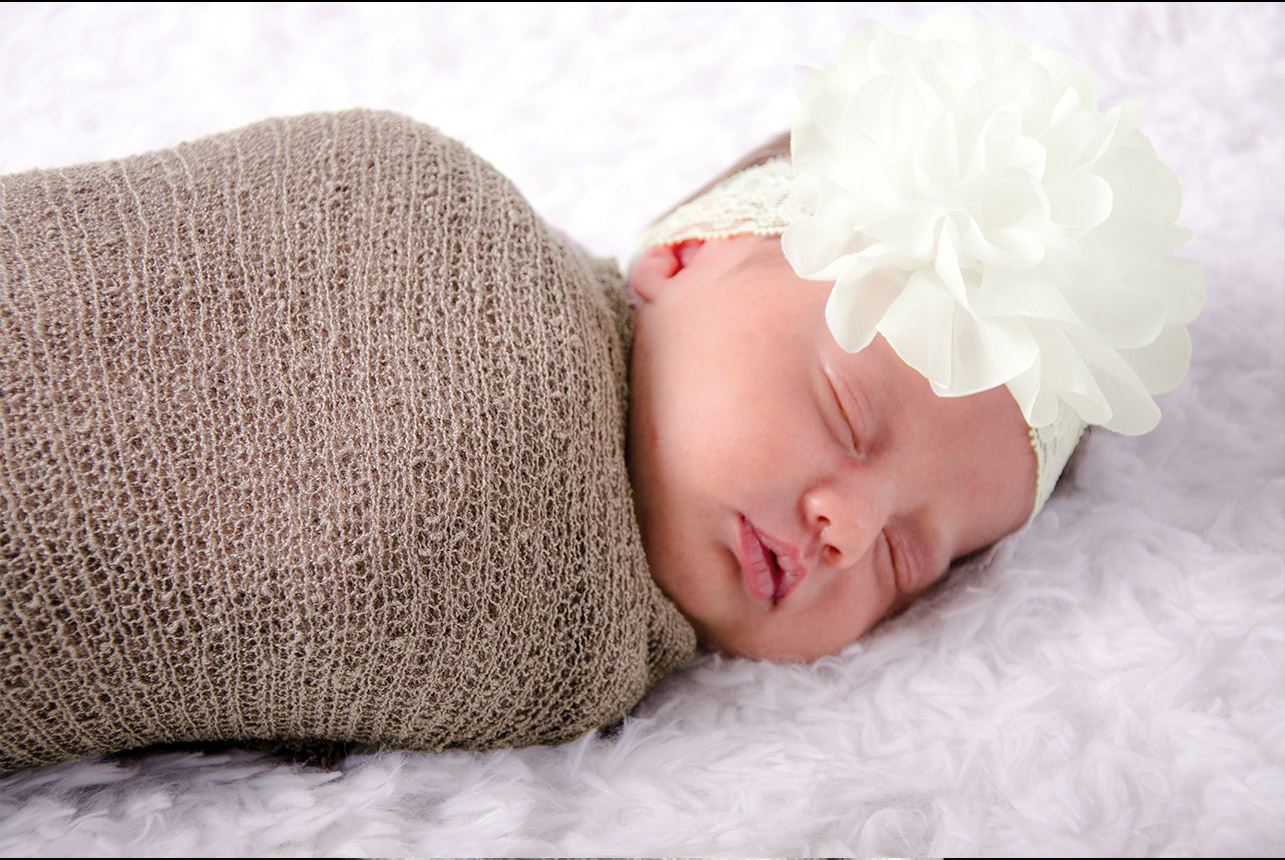 Newborn-toupee-wrap-with-ivory-bow Serene newborn girl sleeping on luxurious faux bedding, wrapped in a soft toupee with an ivory bow