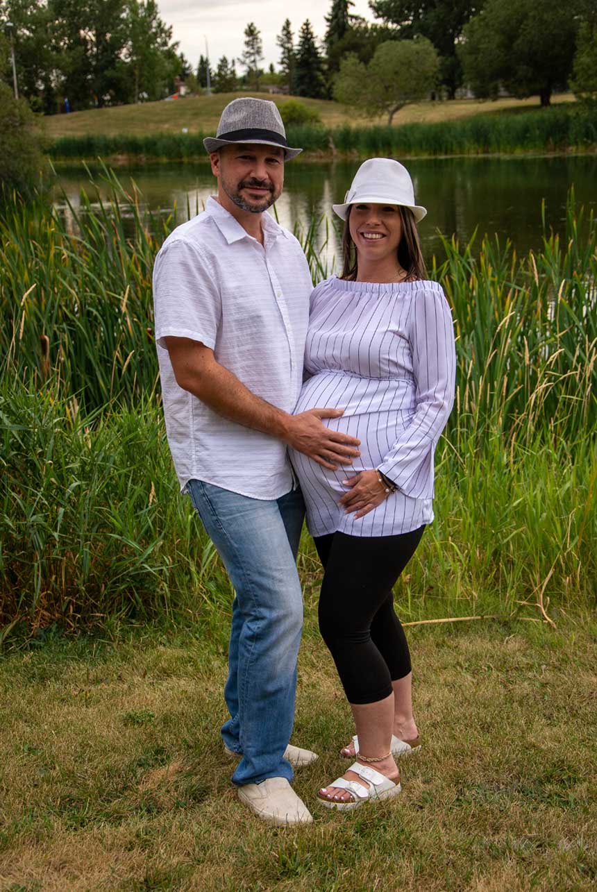 Outdoor maternity photography of a couple with the woman's hand resting on her belly, surrounded by lush greenery in Sherwood Park.