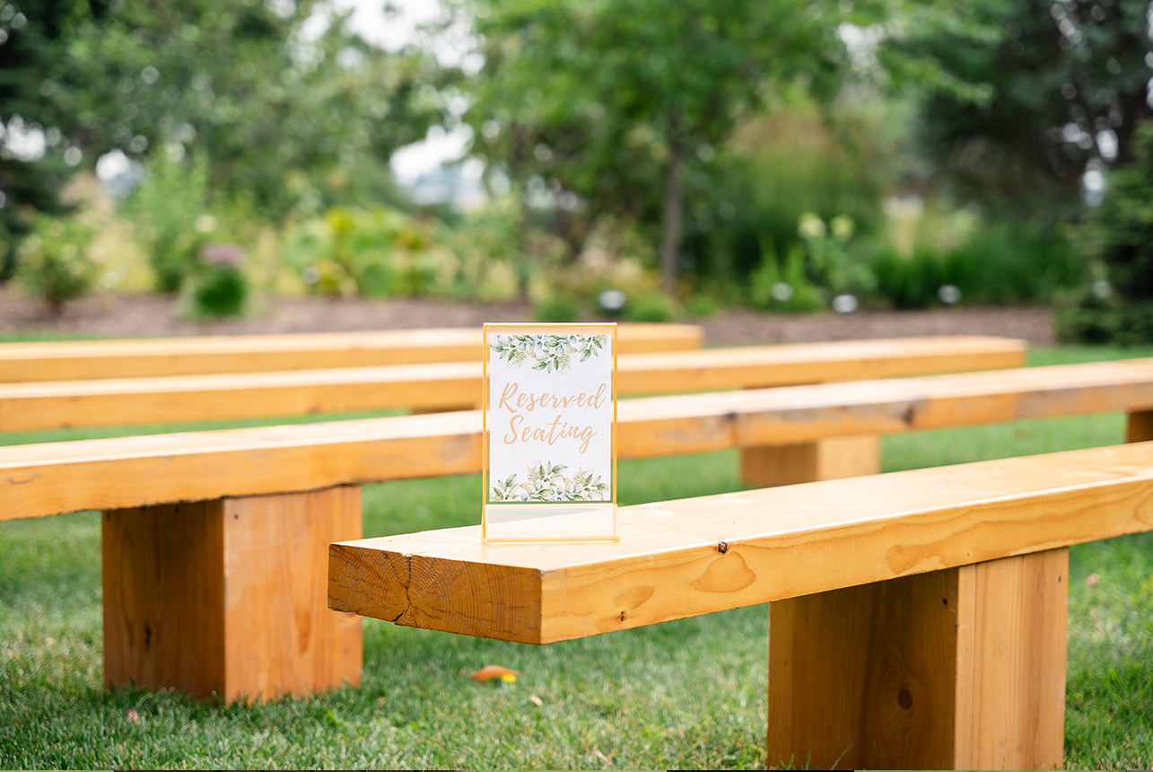 Solid wood benches arranged as reserved seating for an outdoor summer wedding ceremony.