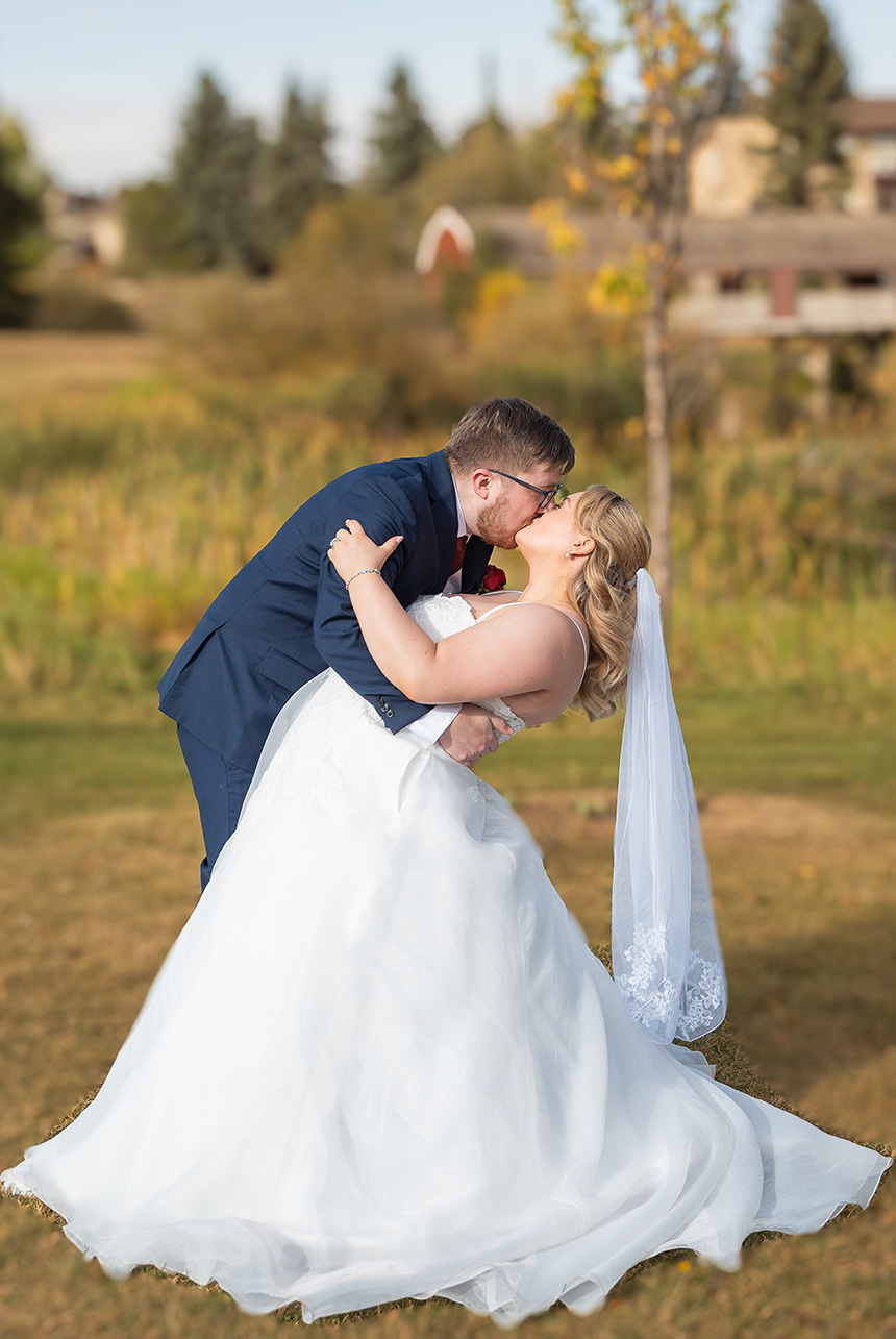 Groom dips his bride for a kiss on the lawn, flowing gown and long veil