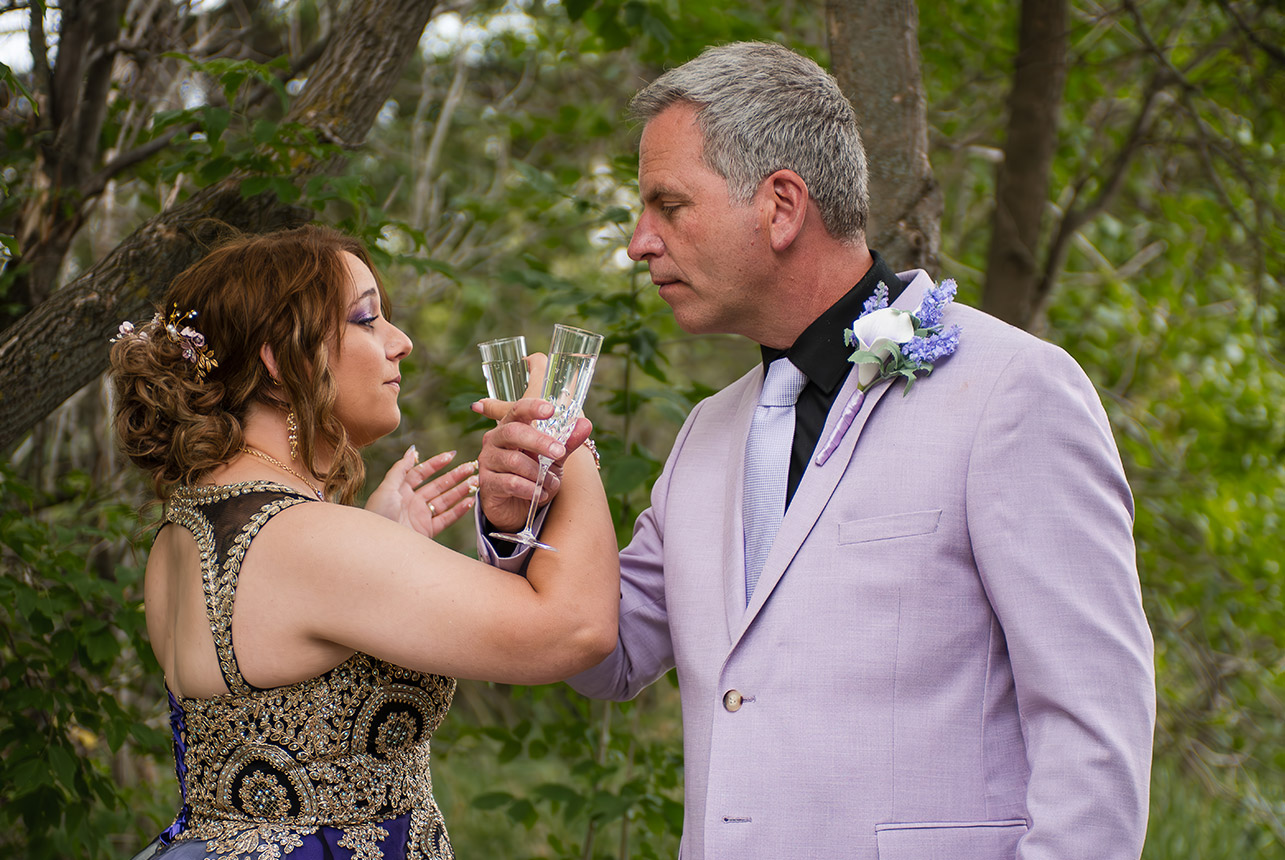 Wedding couple sharing a toast in nature, crossing arms while sipping wine.