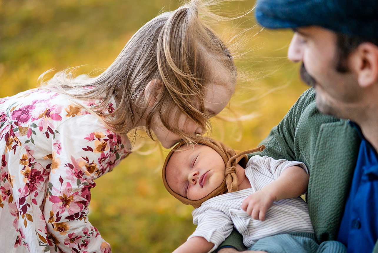 Little girl kissing her newborn baby brother during an autumn family session in Edmonton