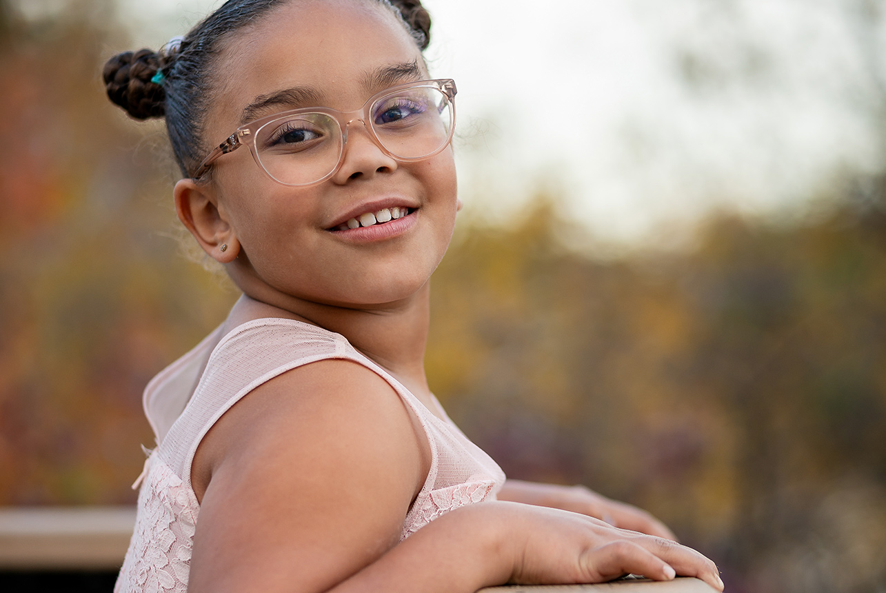 Young girl smiling in pink dress and glasses with soft autumn tones in the background