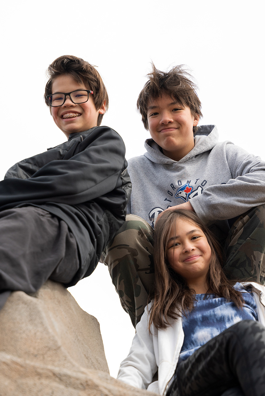 Three siblings smiling on a rock during an outdoor family session in Edmonton