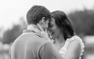 Bride-to-be laughs softly with her fiancé as they lean in forehead to forehead in a tender black and
