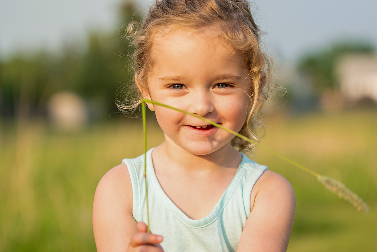 Playful toddler smiling behind a grass stem in River Valley