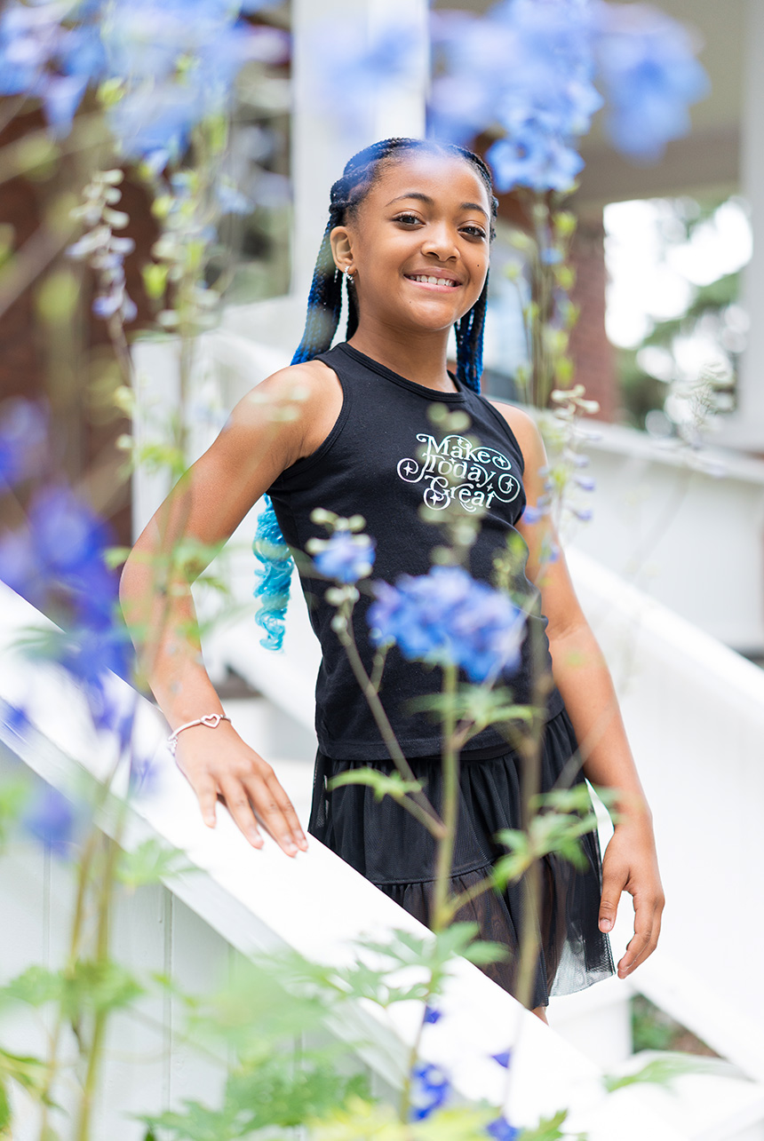 Tween girl smiling through blue flowers at Smeltzer House