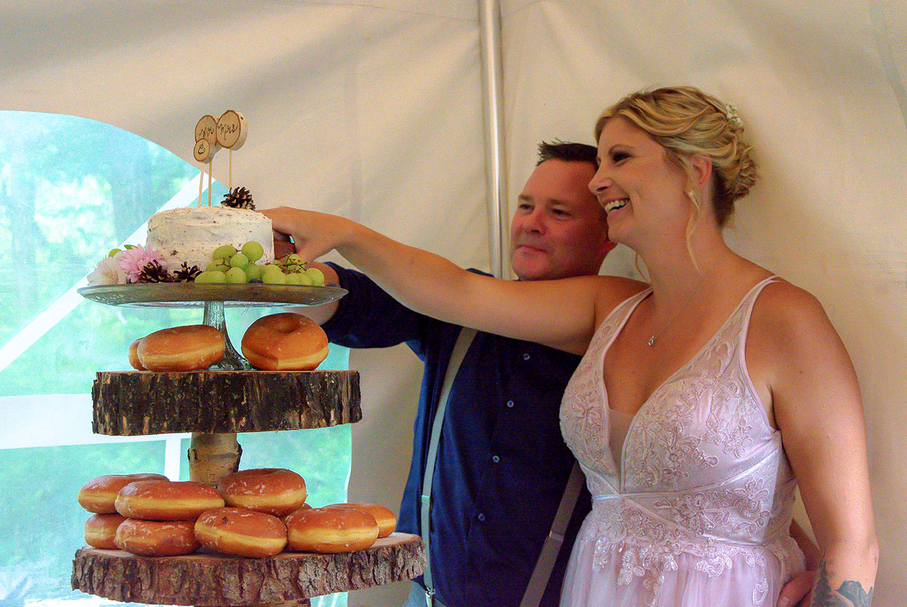 wedding-cake-donut-display Bride and groom cutting their rustic cake and donut display at indoor wedding reception