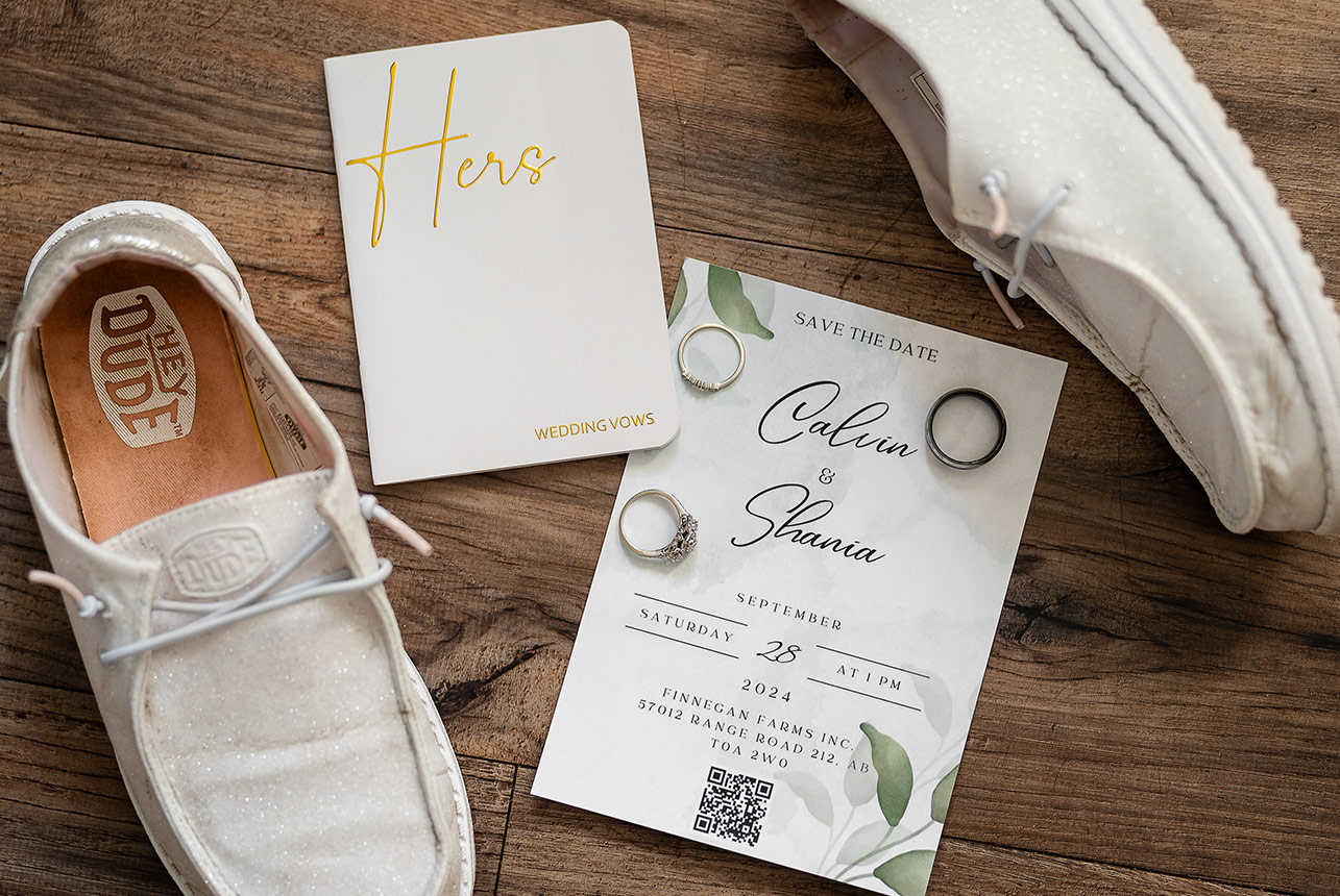 Wedding details including rings, vows, invitations, and shoes arranged on a rustic wooden floor