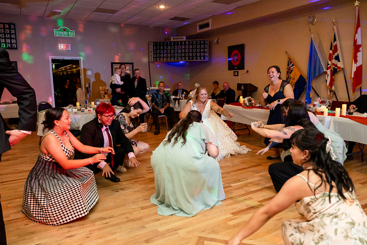 Guests crouch together in unison on the dance floor during a fun and energetic moment at the wedding reception