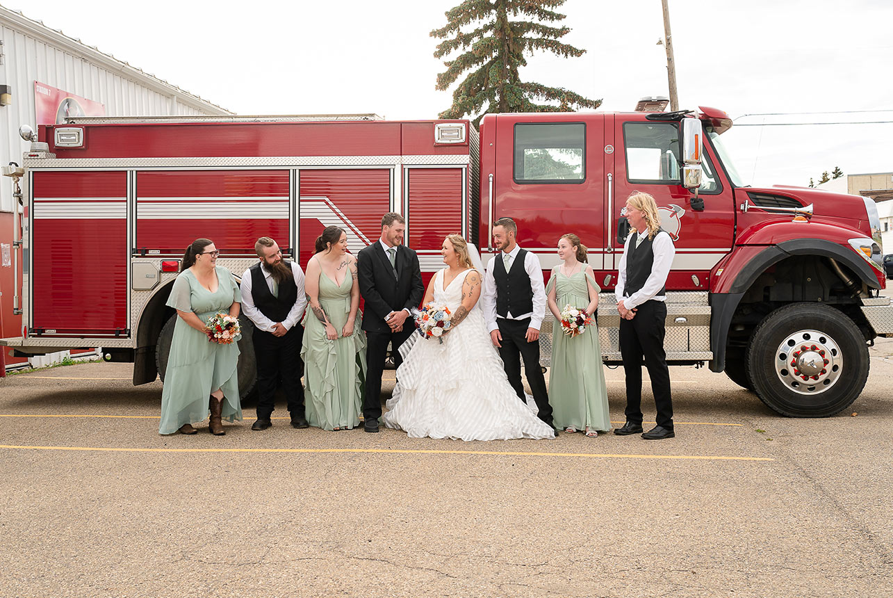 Wedding party poses with the bride in front of a firetruck, celebrating the day in Redwater, Alberta