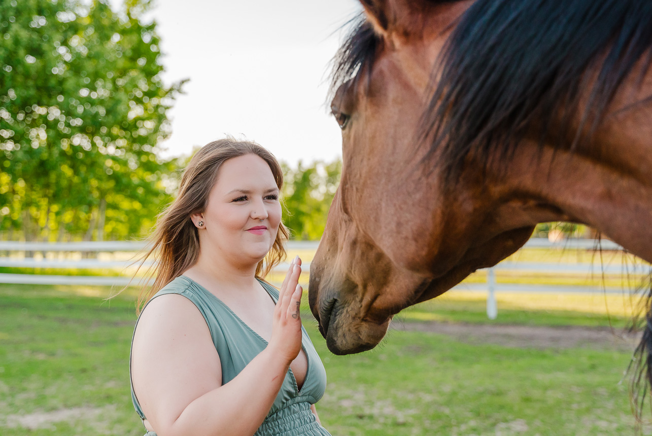 Woman gently raising her hand to greet a horse at Finnegan Farms, smiling in a moment of trust and connection